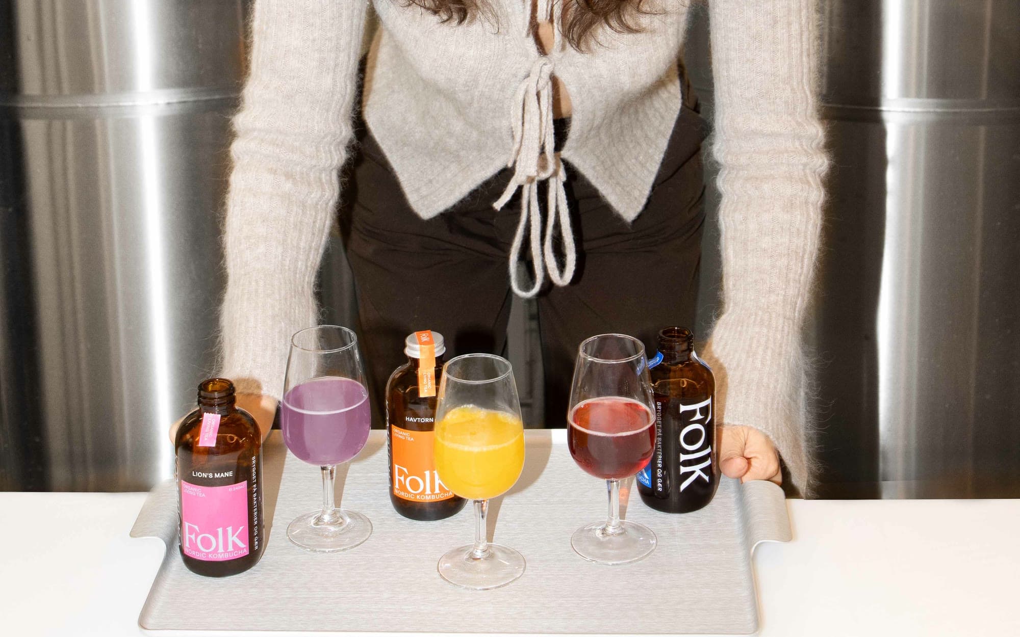 Ochutnávka v pivovaru: lahve Folk Kombucha a sklenice tří příchutí na podnosu